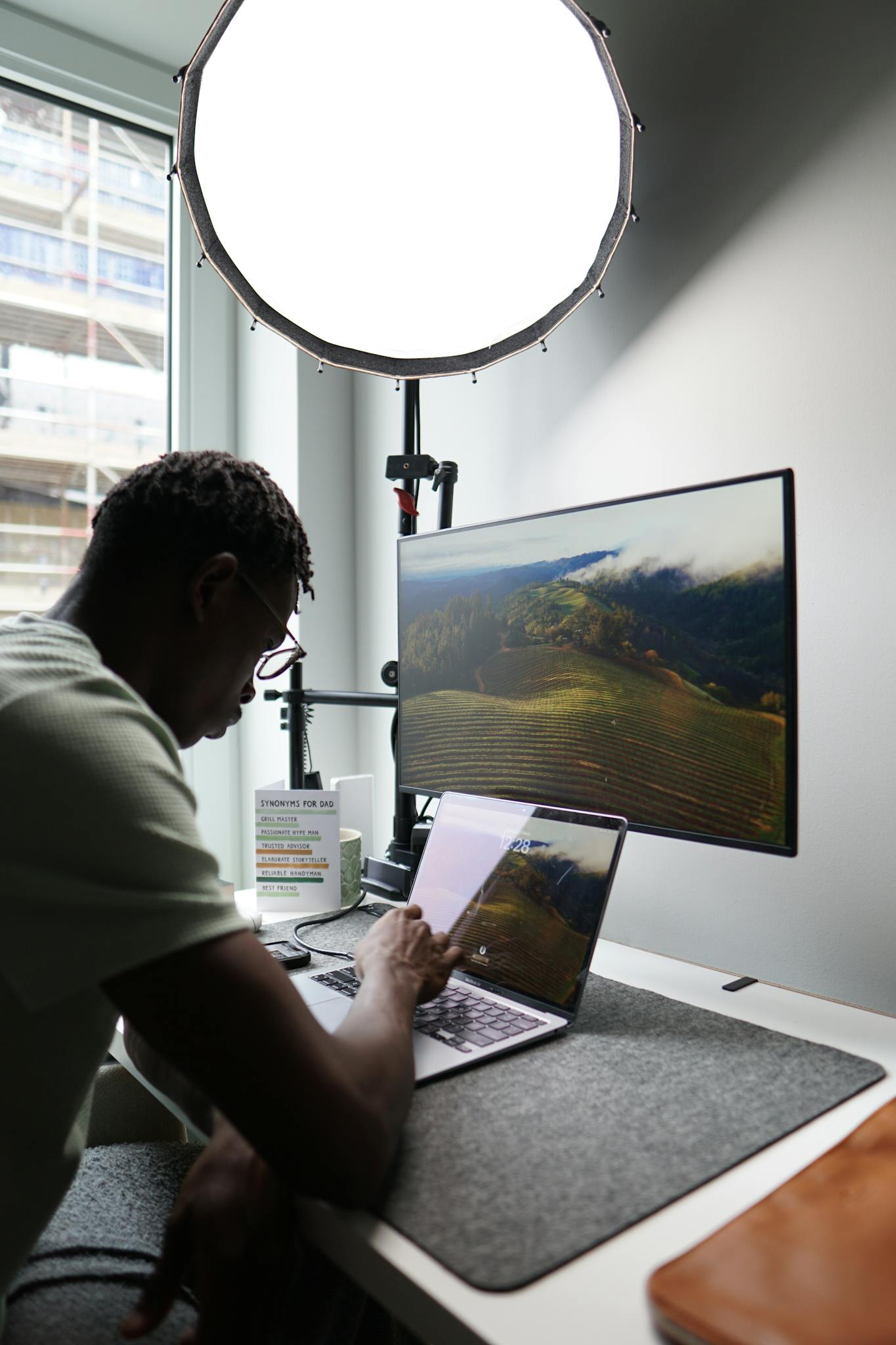 Contemporary home office setup with laptop and large monitor, featuring natural outdoor view through the window.